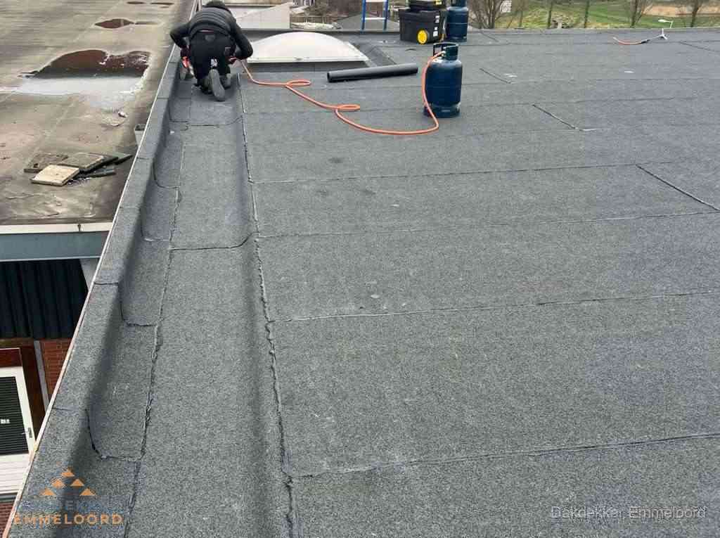 Dakdekker repareert bitumen dakbedekking op groot plat dak in Emmeloord